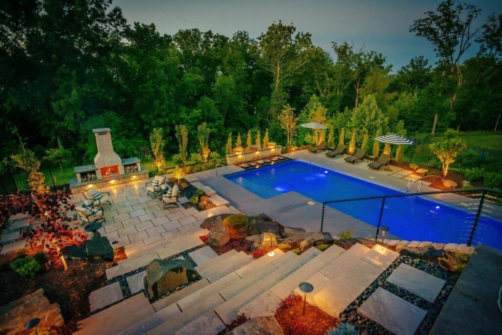 view of outdoor pool and fireplace from top of stairs